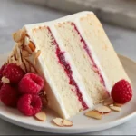 A slice of Raspberry Almond Cake topped with fresh raspberries and almond slivers.