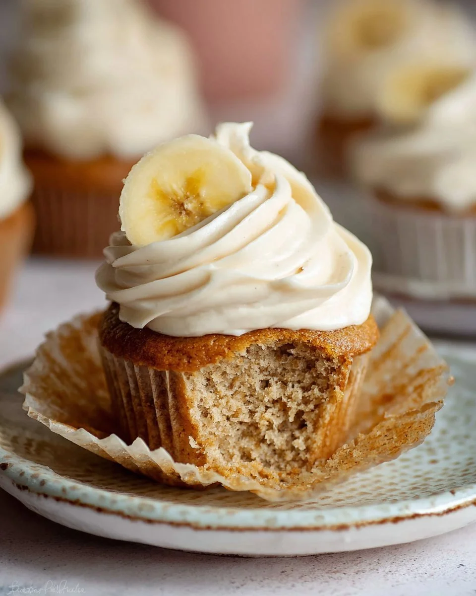 Delicious banana cupcakes with cinnamon cream cheese frosting on a white plate.