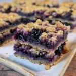 Delicious blueberry crumble bars on a plate with fresh blueberries